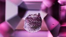 A strikingly textured crystal, likely a metal sulfide, is suspended within a pink spinel; viewed under darkfield and diffuse fiber-optic lighting. The step-cut facets on the stone’s pavilion provide a sense of depth to the image. Photomicrograph by E. Billie Hughes; field of view 3.4 mm.