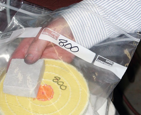 A jeweler placing a yellow platinum polishing wheel labeled “800” and compound into an individual storage bag also labeled “800” 